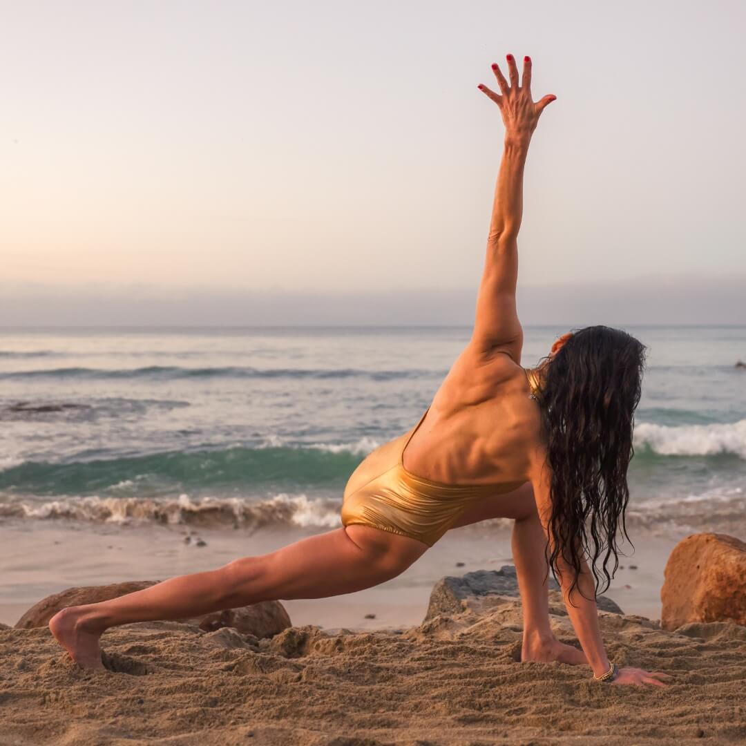 A woman practicing yoga on a beach.